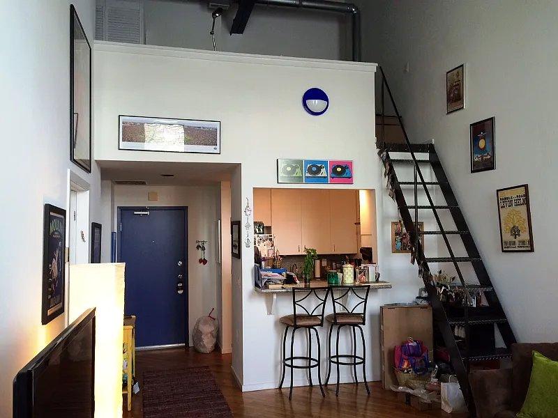 Unit 201 loft entry view with blue front door and metal staircase to mezzanine