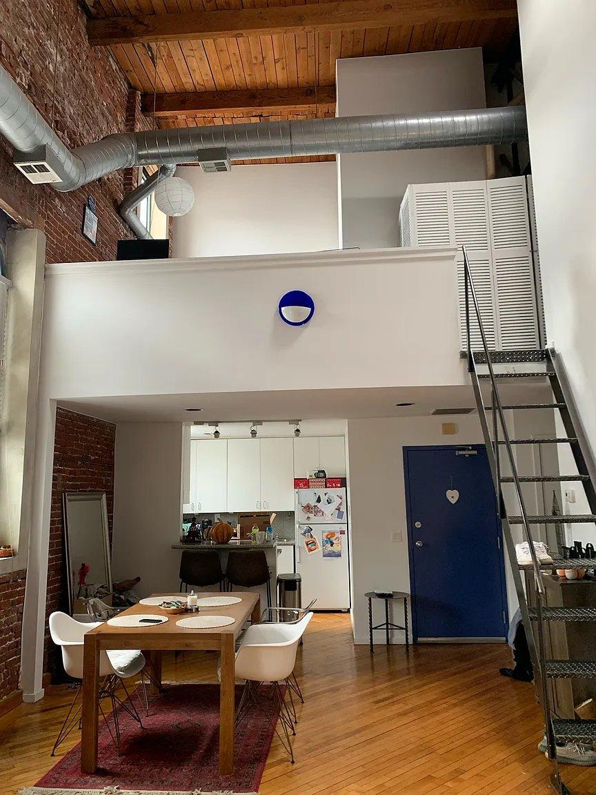 Two-story loft apartment at Cotton Hill — soaring exposed-beam ceilings, full-height brick, private staircase to mezzanine